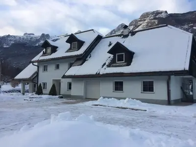 a house covered in snow with mountains in the background at Apartments Alpha Center in Bovec