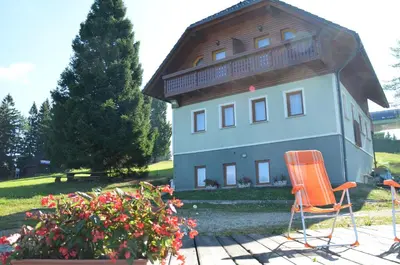 a house with a wooden roof and two chairs and flowers at Apartmaji Srnca in Cerkno