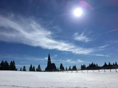a church in the snow with the sun in the sky at Apartment Gaber 82 in Zreče