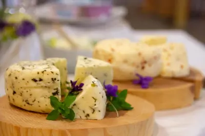 a bunch of cheese on a wooden plate with flowers at Wellness Hotel Montis in Mozirje