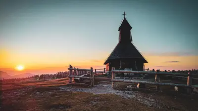 a church on a hill with the sunset in the background at Chalet Resa - Velika planina in Stahovica