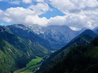 a paraglider flying over a valley in the mountains at Juvanova hiša - Apartments and Rooms in Luče