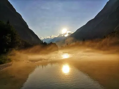 a misty river with the sun in the mountains at Apartment Joži in Soča