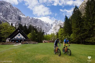 two people riding bikes in a field in front of a lodge at Apartment Katarina Kranjska Gora in Kranjska Gora