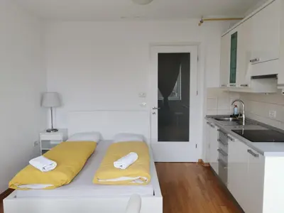 a white kitchen with a bed with yellow pillows on it at Trnovo apartment with free parking in Ljubljana