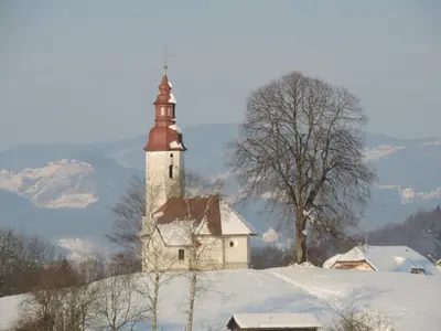 an old church on top of a snow covered hill at Villa Katarina in Mokronog