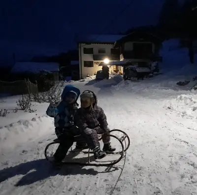 two children sitting on a sled in the snow at Jelenov breg pod Matajurem in Kobarid