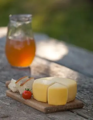 a block of cheese on a cutting board next to a drink at Janezinovi House in Ratečevo Brdo
