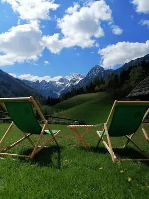 two lawn chairs sitting in a field with mountains at Tourist farm Gradišnik in Solčava