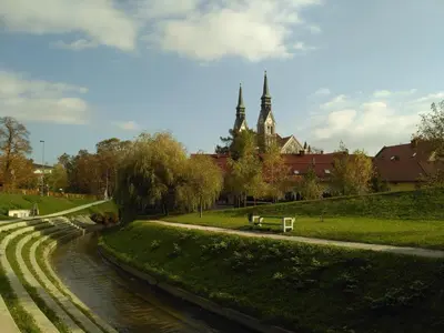a park with a river and a bench and a church at Emona Guesthouse Ljubljana in Ljubljana