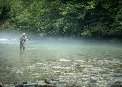 a man is standing in a river holding a string at Farm Stay Loger in Ljubno