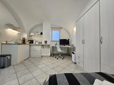a room with a kitchen and a desk with a computer at Tiny central studio apartment Nika Ljubljana in Ljubljana