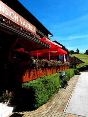 a restaurant with red umbrellas and flowers on a building at Penzion Valerija in Zgornje Jezersko
