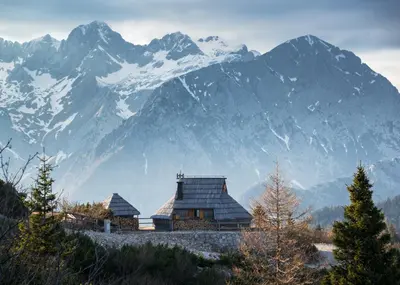 a large snow covered mountain in front of a house at Koča Ojstrica - Velika planina in Stahovica
