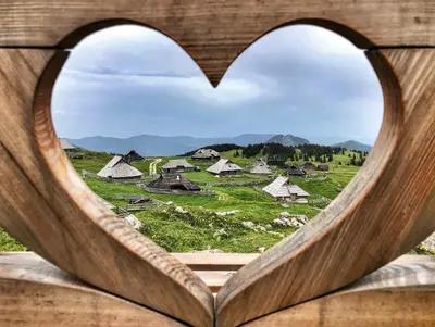 a heart shaped window with a view of a village at Koča Ojstrica - Velika planina in Stahovica
