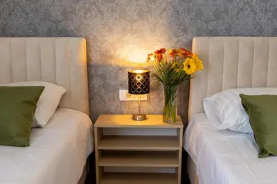 two beds with a vase of flowers on a table with a lamp at Hotel Dolenjc in Novo Mesto