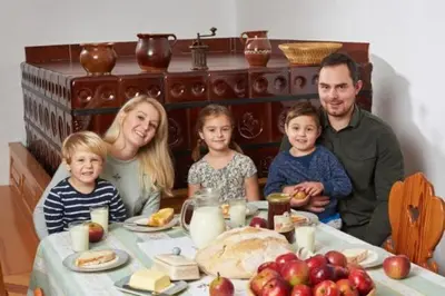 a family is sitting at a table with food at Apartma Lesjak - pobeg v naravo 2 in Šmihel nad Mozirjem
