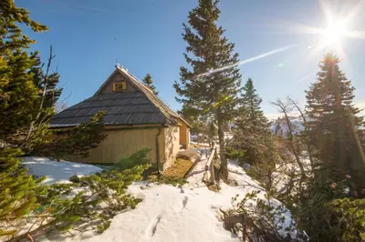 a cabin in the snow with the sun in the background at Chalet Košutnik Velika planina in Kamniška Bistrica
