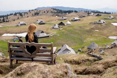 a woman sitting on a bench looking at a village at Chalet Košutnik Velika planina in Kamniška Bistrica