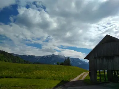 a barn on the side of a field with mountains at Apartmaji Pr-Gujlu Sela nad Podmelcem 5220 TOLMIN in Podmelec