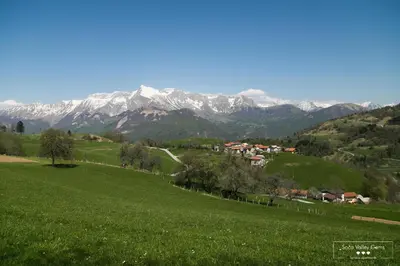 a green field with snow covered mountains in the background at Amber STUDIO in Kobarid