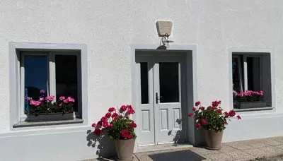 a white building with three windows with flowers in them at House Natura with garden in Bovec