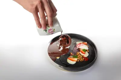 a person pouring chocolate on a plate of food at Hiša Linhart, Hotel & Restaurant in Radovljica