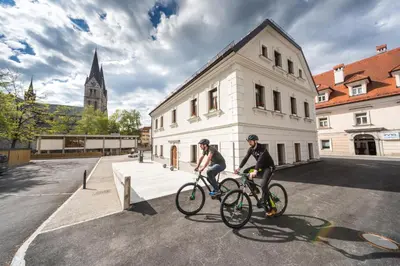two people riding bikes in front of a building at Hostel Bearlog Kočevje in Kočevje