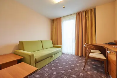 a hotel room with a green couch and a desk at Hotel Korosica in Šentjanž pri Dravogradu
