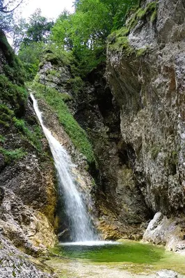 a waterfall on the side of a mountain with green water at Apartma pod Rožem in Soča