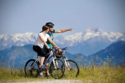 two people riding bikes on a hill with mountains in the background at Alpska perla Apartments in Cerkno