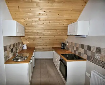 a kitchen with white cabinets and a wooden wall at Apartments Pikon in Bohinj