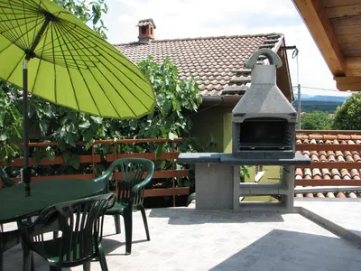 a patio with a grill and a table and chairs with an umbrella at Apartma Furlan in Štanjel