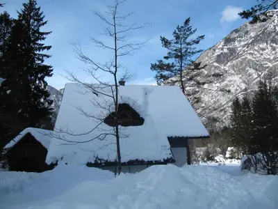 a barn covered in snow with trees and mountains at Apartmaji Zupančič in Bohinj