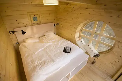 a bed in a wooden room with a round window at Green Resort Glamping in Radlje ob Dravi