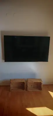 a large flat screen tv on a white wall with two wooden tables at Cozy little nest, Bled region in Jesenice