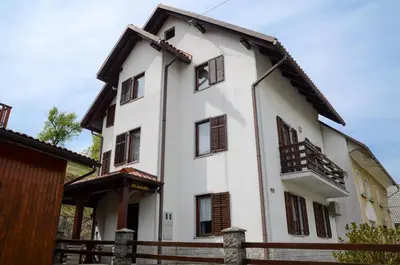 a white house with wooden windows and a fence at Apartment pri Damijanu in Ponikve