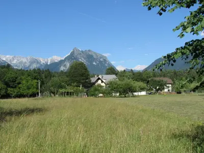 a field with a house and mountains in the background at Apartma Narnia in Bovec