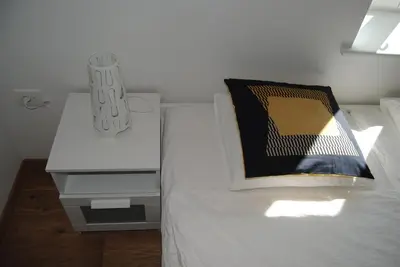a white bed with a black and yellow pillow and a nightstand at Apartment with Free Parking in Ljubljana