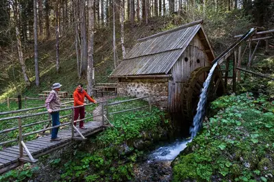 a man and woman standing on a bridge near a mill at Glamping FOREST EDGE in Kamnik