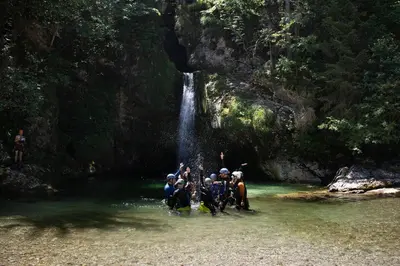 a group of people crossing a river in front of a waterfall at Hostel pod Voglom in Bohinj
