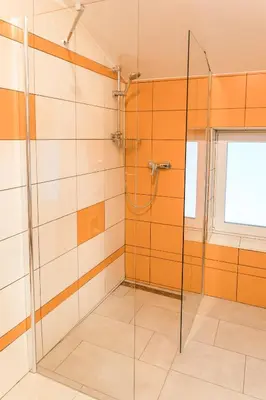 a glass shower in a bathroom with orange and white tiles at Guest House Rosi in Tolmin