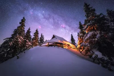 a cabin in the snow at night with the milky way at Koča Bistra - Velika planina in Stahovica