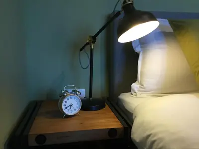 a lamp and an alarm clock on a wooden table next to a bed at Apartmaji 43 in Tolmin