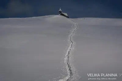 a snow covered hill with a trail in the snow at Koča Predilnica Velika Planina in Kamniška Bistrica