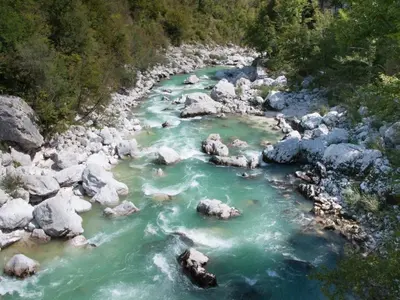 a river with rocks and green water and trees at Apartma Matajurc in Trnovo ob Soči