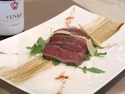 a piece of meat on a plate with a bottle of wine at Hotel Venko in Dobrovo