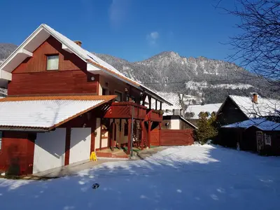 a house in the snow with mountains in the background at Zajček Apartma in Mojstrana