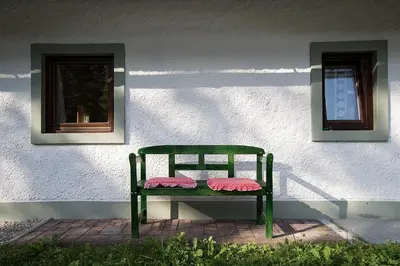 a green bench sitting in front of a building with two windows at Holiday Home Voje in Bohinj