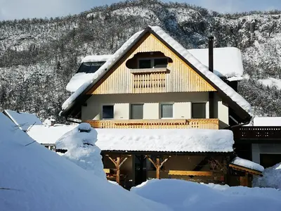 a house covered in snow with a mountain in the background at TriSa apartments Bohinj in Bohinj